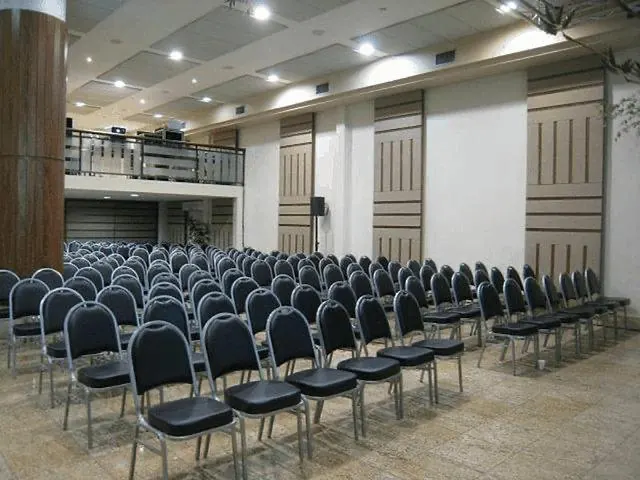 Salão com cadeiras em fileiras, mezanino e painéis de madeira nas paredes
